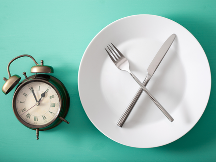 a plate with a fork and knife next to an alarm clock.