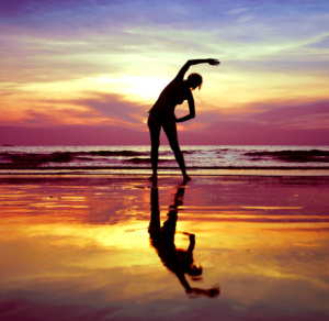 A silhouette of a woman doing yoga on the beach at sunset.