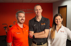 Three people in orange shirts standing in front of an orange wall.